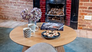 Una mesa redonda de madera con dos tazas de café estampadas, un libro titulado 'The History of the 487th Bomb Group (H)' y un plato de tartaletas de cereza.