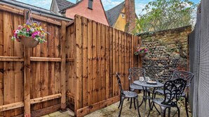 Una valla de madera, un muro de piedra y una mesa con sillas en un patio.