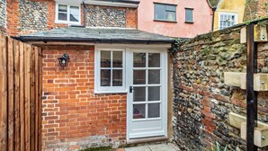 A small brick house with a white door and windows, a stone wall, and a wooden fence. - 2 Bed in Lavenham (oc-s30055) (Lavenham)