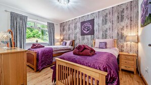 Une chambre avec deux lits, un bureau en bois et une grande fenêtre.