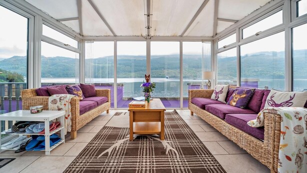 Une pièce spacieuse avec deux canapés en osier, une table basse et une vue sur un lac et des montagnes.