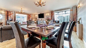Un espace repas avec une grande table en bois, dressée pour six personnes, entourée de fauteuils en cuir.