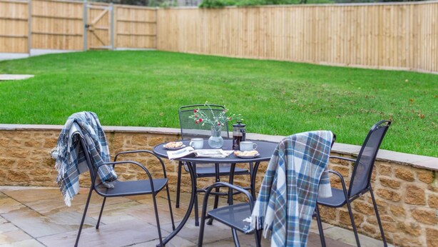 A patio with a table set for two, surrounded by stone walls and a wooden fence. - 2 Bed in Melplash (oc-r30043) (Melplash)