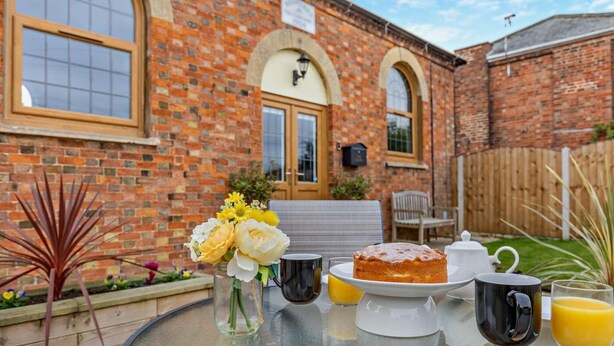 Une table dressée à l’extérieur, avec un gâteau, une théière, une tasse et un verre de jus d’orange.