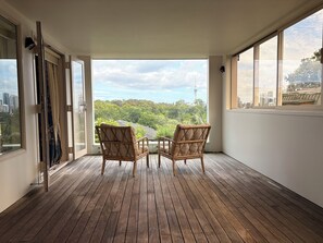 A balcony with two wicker chairs, wooden flooring, and a view of a cityscape and greenery. - Luxury Parnell Pad (Parnell)