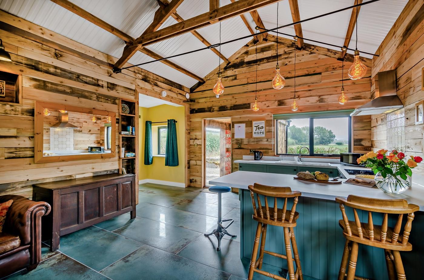 A rustic kitchen with wooden walls, a large island with bar stools, and a view through the window.