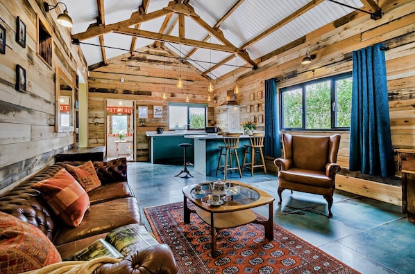 A rustic cabin interior with a leather sofa, a coffee table, a wooden dining area, and a kitchen.