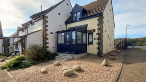 A two-story house with a dark blue front door, stone pillars, and a gravel driveway. - 2 Bed in Padstow (oc-t30052) (Padstow)