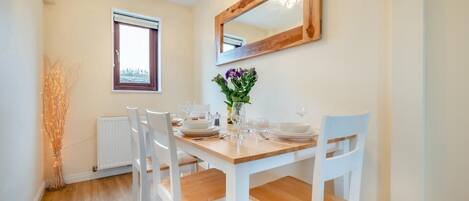 A dining area with a wooden table, white chairs, a vase with flowers, and a mirror on the wall.