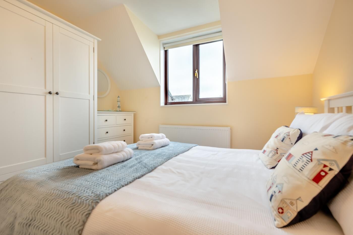 Un dormitorio con cama, ventana, armario y mesita de noche.