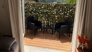 Een balkon met rieten stoelen en een tafel, een houten terras en uitzicht op heuvels en een afrastering.