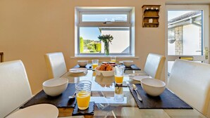 Een eettafel gedekt voor vier personen, met kommen, glazen en een vaas met bloemen.