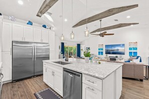 A modern kitchen with stainless steel appliances, a large island, pendant lighting, and a ceiling fan. - 120 S 5th Street (Cocoa Beach)