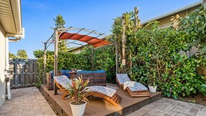 Eine Terrasse mit Holzboden, zwei Liegestühle, einem Grill und einer Pergola mit rotem Baldachin.
