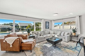 Uma sala de estar ampla, com um sofá grande, uma mesa de centro e vista para a piscina e área externa.