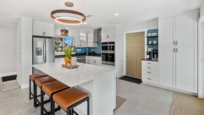 Une cuisine moderne avec des meubles blancs, un îlot central doté de tabourets et un luminaire suspendu.