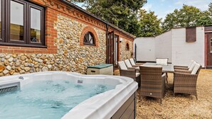 A spa area with a hot tub, wicker furniture, and a stone wall. - 4 Bed in Litcham (oc-h30106) (Litcham)