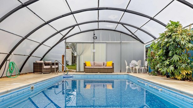 A pool area with a glass ceiling, a sofa, and chairs. - 4 Bed in Litcham (oc-h30106) (Litcham)
