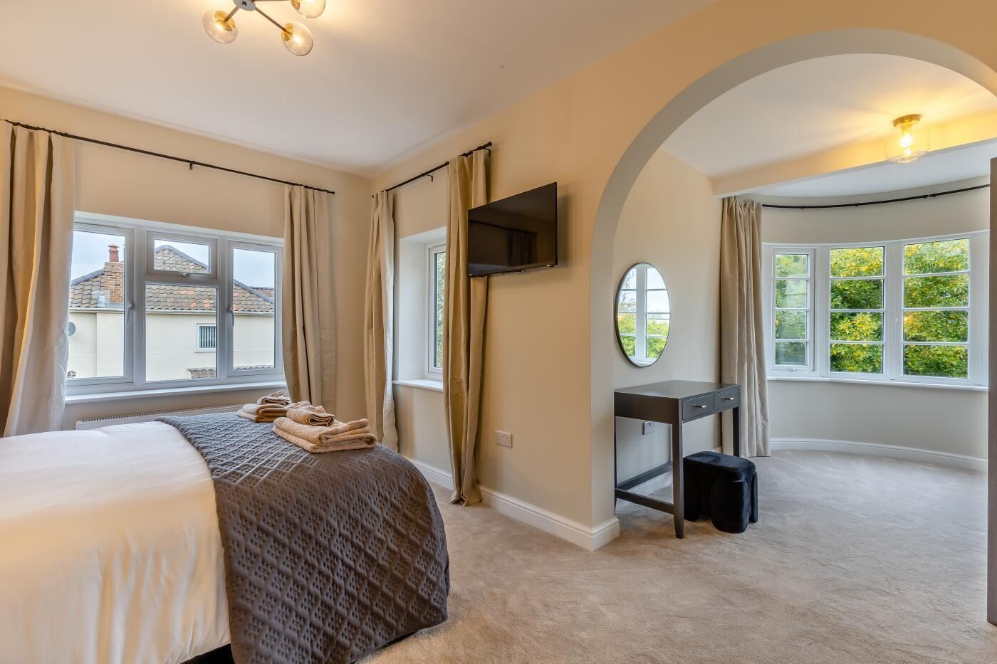 A bedroom with a bed, a desk, a TV, and a large window with curtains.