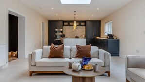 A modern living room with a sofa, a coffee table, and a kitchen in the background. - 4 Bed in West Runton (oc-c30082) (West Runton)