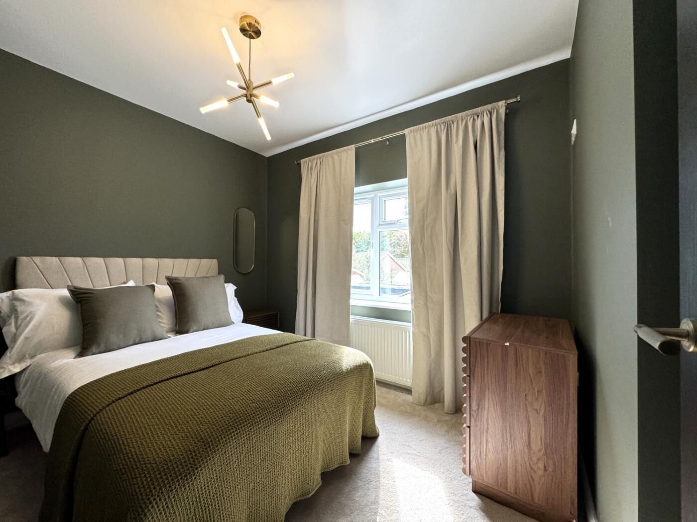 A bedroom with a bed, a wooden cabinet, and a window with curtains.