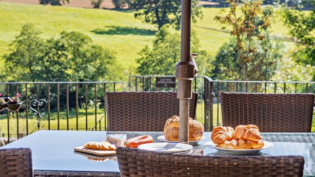 A table set outdoors with wicker chairs, a metal railing, and a view of a green field. - 4 Bed in Ellastone (oc-11744sf) (Ellastone)
