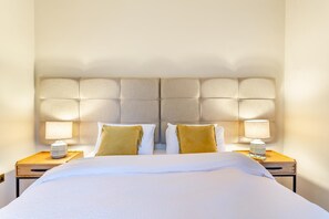 Hotellihuone, jossa on suuri sänky, kaksi yöpöytää ja pääty, jossa on kuvioitu, napitettu verhoilu.