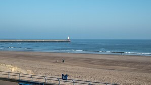 A beach with a lighthouse in the distance, a clear sky, and a few people walking along the shore. - 2 Bed in Spittal (oc-b30119) (Spittal)
