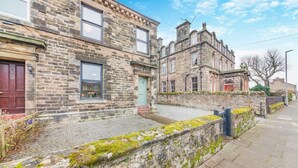 A stone building with a traditional design, featuring a mix of rectangular and arched windows, a prominent entrance with a red door, and a small porch area. - 2 Bed in Spittal (oc-b30119) (Spittal)