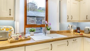 A kitchen with white cabinets, a wooden countertop, a window with a view of buildings, a sink, a toaster, and a tray with baked goods. - 2 Bed in Spittal (oc-b30119) (Spittal)