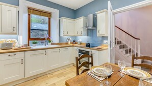A modern kitchen with white cabinets, a wooden countertop, and a dining area with a table set for two. - 2 Bed in Spittal (oc-b30119) (Spittal)