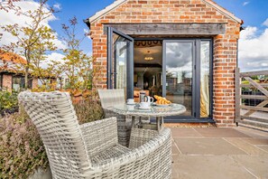 Un bâtiment en briques avec une porte en verre et une table en osier entourée de chaises, le tout installé à l’extérieur.