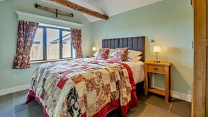 Quarto com cama grande, cabeceira de madeira, mesa de cabeceira com abajur e janela com cortinas.