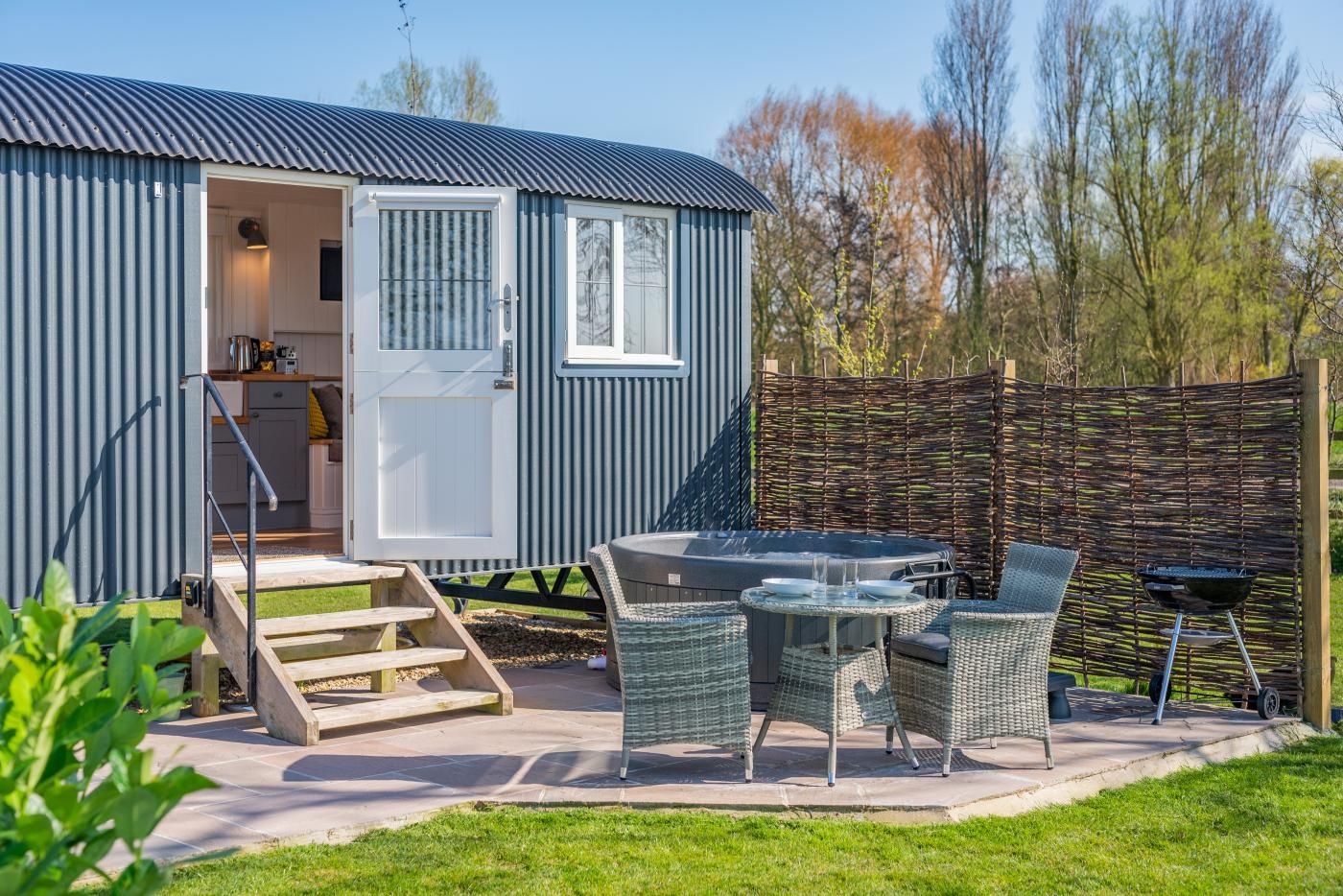 Une maison mobile dotée d’un patio comprenant un jacuzzi, des meubles en osier et un barbecue.