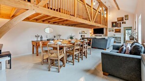 A spacious loft with exposed wooden beams, a dining area with a round table, and a cozy seating area with a sofa. - 5 Bed in Sedlescombe (oc-c30096) (Sedlescombe)