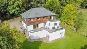 Uma casa moderna de dois andares com telhado plano, grandes janelas e uma varanda.