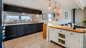 Une cuisine moderne avec des meubles de couleur sombre, un plan de travail en bois et des luminaires suspendus.