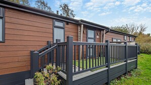 Une maison mobile moderne, avec une façade en bois, une clôture en métal noir et un petit jardin.
