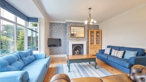 Een woonkamer met een blauwe bank, een blauwe fauteuil, een houten salontafel en een open haard.