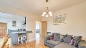 Een moderne woonkamer met een grijze bank, houten vloeren en een keuken op de achtergrond.