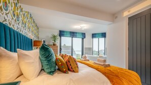 Une chambre d’hôtel avec un lit, des oreillers, une table de chevet, une fenêtre donnant sur un paysage agréable et une porte.