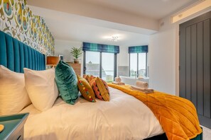 A hotel room with a bed, pillows, a bedside table, a window with a view, and a door. - 4 Bed in Carbis Bay (oc-r30048) (Carbis Bay)
