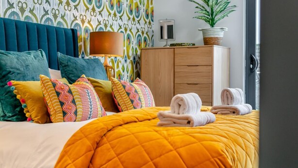 Une chambre d’hôtel avec un lit, une table de chevet, une lampe, une plante en pot et une armoire en bois.