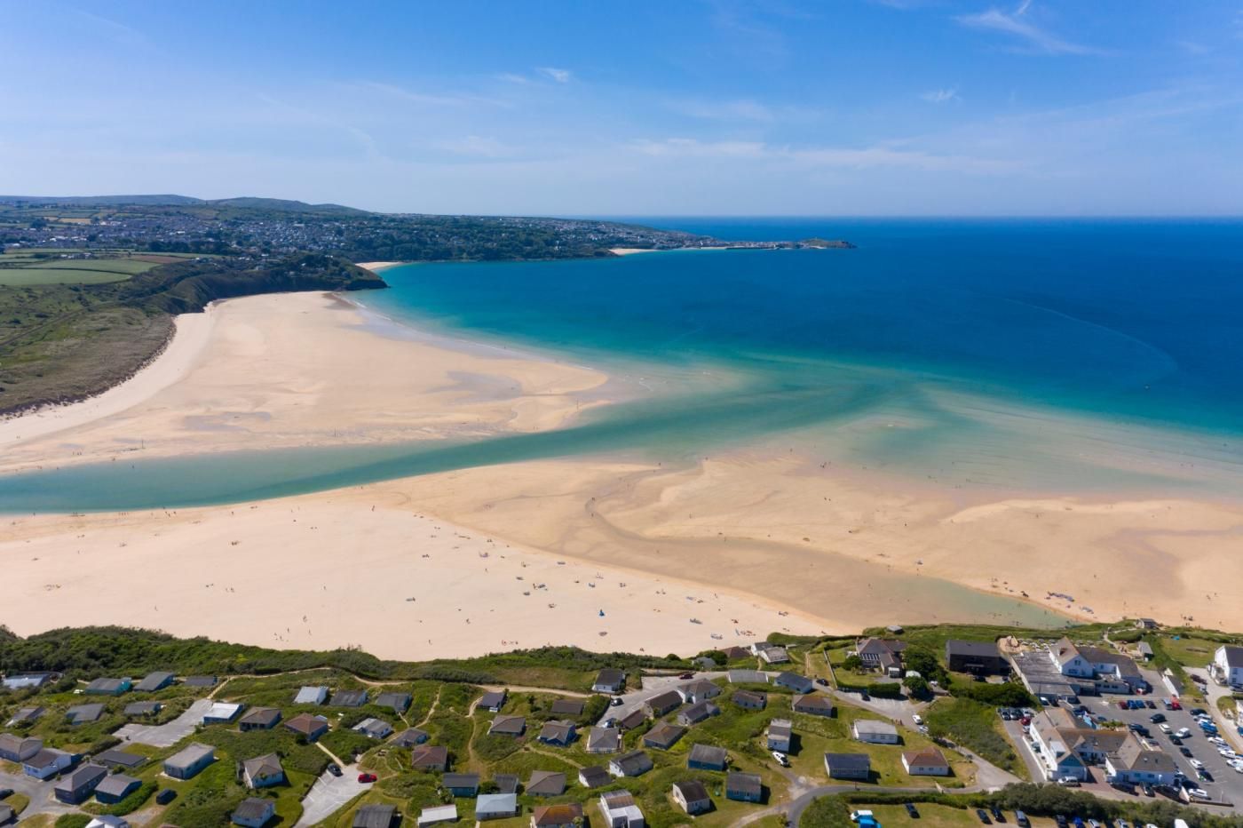 Vue aérienne d’une zone côtière avec une plage de sable, une petite ville avec des maisons et une mer bleue et limpide.