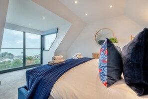 A bedroom with a large bed, a skylight, a view of the outside, and a round mirror on the wall. - 4 Bed in Carbis Bay (oc-r30048) (Carbis Bay)
