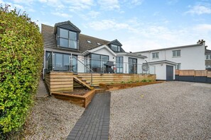 Ein modernes Haus mit einer Holzdiele, einem Schotterweg und blauem Himmel.