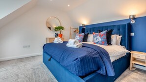 Une chambre à coucher avec un grand lit, une table de chevet, une commode, un miroir, une plante en pot et un luminaire au plafond.