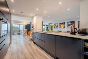 A modern kitchen with a central island, a dining area with a view, and a living space with artwork. - 4 Bed in Carbis Bay (oc-r30048) (Carbis Bay)