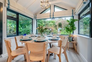 Un espace repas avec une table dressée pour six personnes, entouré de grandes fenêtres offrant une vue sur la verdure.