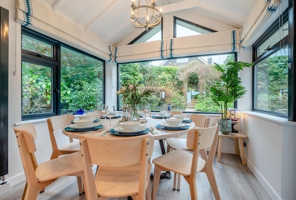 A dining area with a table set for six, surrounded by large windows with a view of greenery. - 4 Bed in Carbis Bay (oc-r30048) (Carbis Bay)